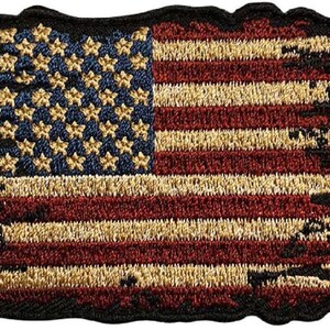 Puede incluir: Un parche rectangular bordado con un diseño de bandera estadounidense desgastada. El parche muestra un campo azul con estrellas doradas y rayas horizontales rojas y doradas, todo bordeado por un grueso borde negro cosido con contorno ondulado.