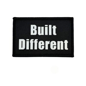 May include: A black rectangular patch featuring the words "Built Different" in bold white lettering. The patch has a black border and is set against a white background. The text is centered.