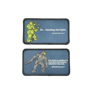 Peut inclure: Deux écussons rectangulaires brodés avec des bordures noires sur fond bleu. L'écusson du haut présente une silhouette blindée vert citron et le texte : Sir... finishing this fight. SPARTAN 117. L'écusson du bas montre une silhouette blindée grise et le texte : Our duty as soldiers is to protect humanity, whatever the cost. SPARTAN 117.