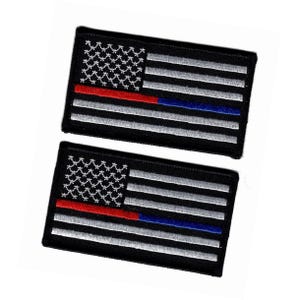 May include: Two rectangular embroidered patches featuring a stylized American flag design. The background is black with white embroidered stars and stripes. A single horizontal stripe is split, featuring a red section and a blue section.