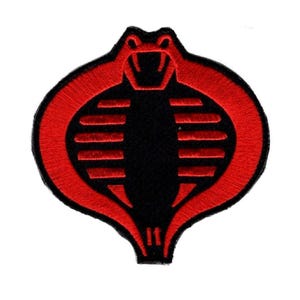 Puede incluir: Un parche bordado circular que presenta un diseño estilizado de cabeza de cobra. El emblema está realizado con hilo rojo vibrante sobre un fondo negro sólido, mostrando una forma de capucha simétrica con rayas rojas horizontales.