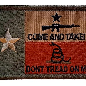 May include: A rectangular embroidered patch featuring a dark olive green vertical stripe with a white star on the left. The right side has a tan top section with a black rifle and star above the text COME AND TAKE IT, and a red bottom section with a black coiled snake above the text DONT TREAD ON ME.