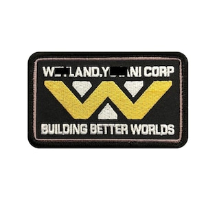 Puede incluir: Un parche rectangular bordado con fondo negro y un borde negro grueso. Presenta una letra W amarilla estilizada grande en el centro, con texto blanco arriba que dice WEYLAND-YUTANI CORP y abajo que dice BUILDING BETTER WORLDS.