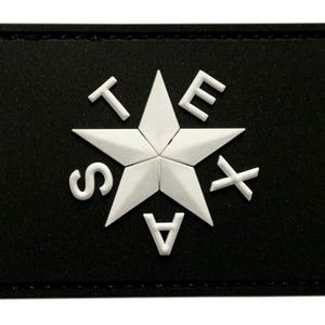 Puede incluir: Un parche rectangular negro que presenta una estrella blanca de cinco puntas en el centro. Las letras T, E, X, A y S están dispuestas alrededor de la estrella en un patrón circular, con las letras en relieve blanco sobre el fondo negro.