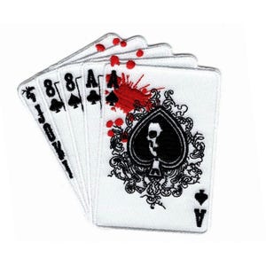 May include: A white embroidered patch shaped like a fan of five playing cards. The cards feature black suits and numbers, with the ace of spades prominently displayed in the front, decorated with a skull and red embroidered blood splatter.