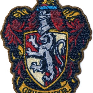 May include: An embroidered patch featuring a shield with a silver lion on a red and cream background. Above the shield is a silver helmet and a crescent moon. The design is surrounded by red and gold flourishes, with the text GRYFFINDOR on a banner.