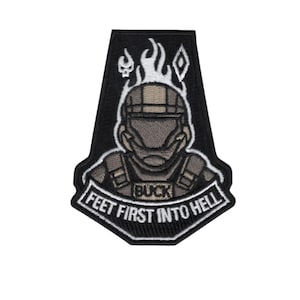 May include: Black embroidered patch featuring a soldier's helmeted face with flames above. The text "BUCK" is above the soldier's chest, and "FEET FIRST INTO HELL" is below.