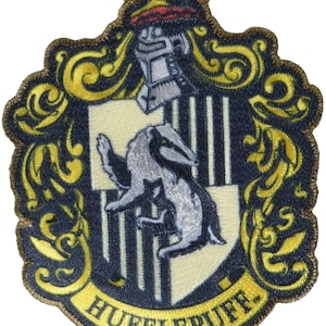 May include: An embroidered patch featuring a crest with a central badger on a black and yellow striped shield. Above the shield is a silver helmet, and below is a yellow banner with the text HUFFLEPUFF in black letters, surrounded by gold scrollwork.