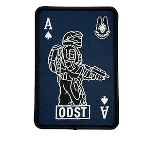 May include: A navy blue patch in the shape of a playing card, featuring a white outline of a soldier holding a gun. The card is the Ace of Spades, with the letters "A" and the spade symbol at the top and bottom. The text "ODST" is at the bottom.