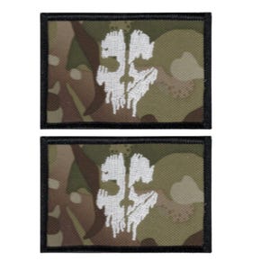 May include: Two rectangular patches with a camouflage pattern in shades of green, brown, and tan. Each patch features a white, stylized skull design. The patches have a black border.