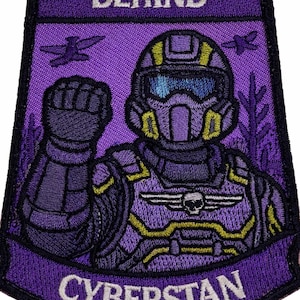 May include: Purple embroidered patch with the text "WE LEFT MEN BEHIND" and "CYBERSTAN". The patch features a futuristic soldier with a raised fist, a skull emblem, and yellow accents. Two stylized aircraft are also present.