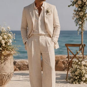 May include: A beige linen suit consisting of a single-breasted blazer with notched lapels and matching wide-leg trousers. The outfit includes a light beige button-down shirt, a small white floral boutonniere, and light beige suede loafers.