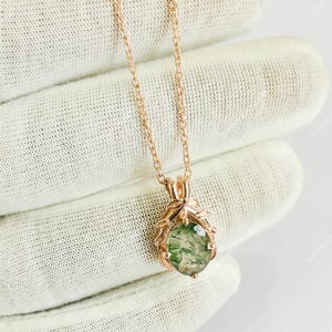 May include: Rose gold necklace featuring a pendant with a green moss agate stone. The pendant is held by a decorative rose gold setting. The necklace is displayed on a white surface.