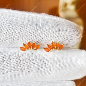 Puede incluir: Un par de pendientes de botón de oro, cada uno con una disposición en abanico de cinco piedras preciosas naranjas de talla marquesa. Las piedras están engastadas en un diseño curvo en forma de corona, creando un aspecto delicado y simétrico.