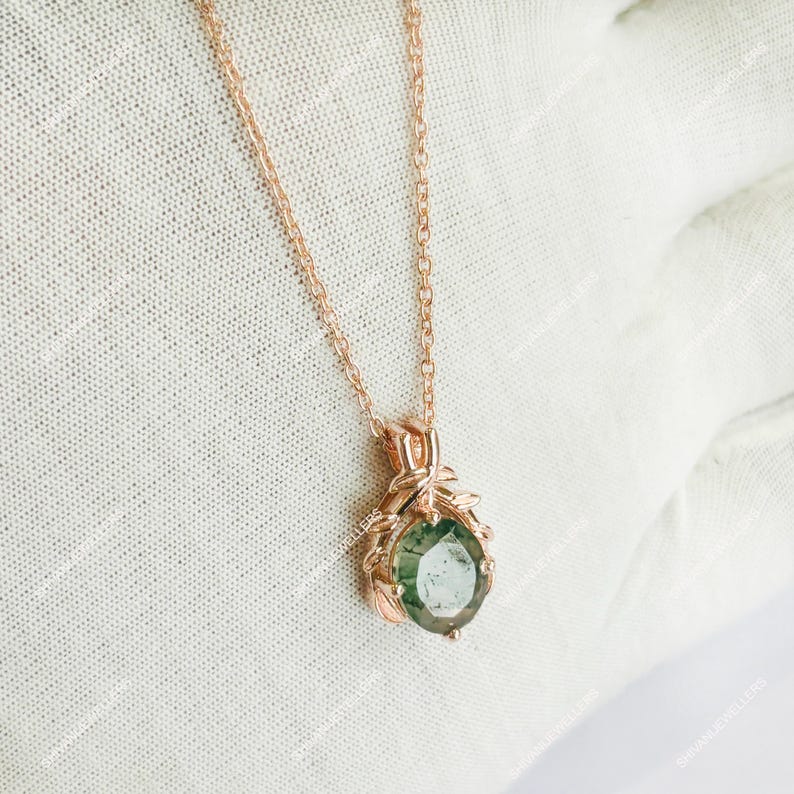 May include: Rose gold necklace featuring a green gemstone pendant. The pendant is a round, faceted stone set in a decorative rose gold setting with leaf-like accents. The chain is delicate and also rose gold.