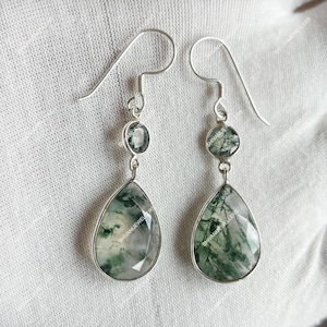 Puede incluir: Pendientes de plata con una piedra verde y blanca en forma de lágrima. Los pendientes tienen un cierre de gancho y una piedra redonda más pequeña encima de la lágrima. Las piedras presentan un patrón natural, similar al musgo.