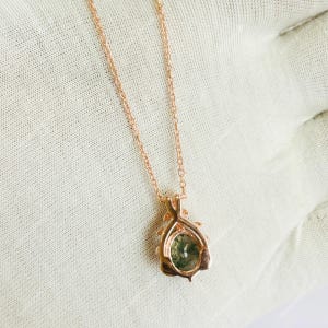 May include: Rose gold necklace with a pendant featuring a green gemstone. The pendant has an oval-shaped green stone set in a decorative rose gold frame. The chain is delicate and also rose gold.