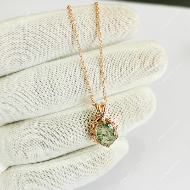 May include: Rose gold necklace featuring a pendant with a green moss agate stone. The pendant is held by a decorative rose gold setting. The necklace is displayed on a white surface.
