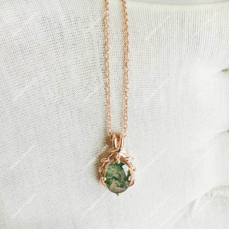 May include: Rose gold necklace featuring a pendant with a green moss agate stone. The pendant is oval-shaped and surrounded by a decorative rose gold frame. The necklace chain is delicate and hangs on a white background.