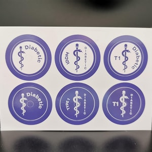 Może przedstawiać: Arkusz z sześcioma okrągłymi naklejkami w niebiesko-białym wzorze. Każda naklejka zawiera symbol laski Asklepiosa i słowo "Diabetic" w kolorze białym, z dodatkowym tekstem, takim jak "IDDM" i "T1".