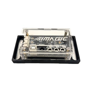 May include: A black and clear electronic device with the text "SIMMAGIC" printed on it. The device is encased in a clear plastic housing and mounted on a black base. It features various ports and connectors.