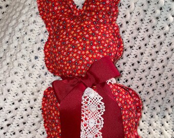 May include: A red fabric bunny with a white lace and burgundy ribbon bow. The bunny is sitting on a white crocheted blanket.