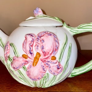May include: White ceramic teapot with a green handle and a floral design featuring pink and purple irises.