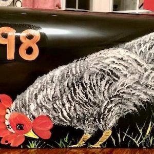 May include: A black mailbox with the number 1098 painted on the front. A painted image of a grey hen with red accents is on the bottom half of the mailbox. The hen is looking down at a nest of eggs.