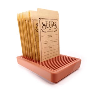 May include: A set of seed packets in a terracotta-colored tray. The packets are tan with the word "SEEDS" in a decorative font. The packets are labeled "FROM THE GARDEN OF" with spaces for "SEED TYPE", "VARIETY", "DATE COLLECTED", and "NOTES".