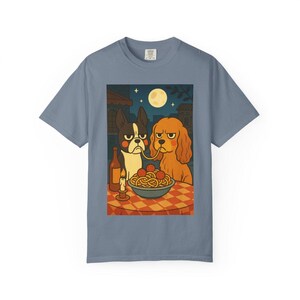 Puede incluir: Camiseta azul con una ilustraci&oacute;n de dibujos animados de dos perros compartiendo espaguetis. La escena incluye una botella de vino, una vela encendida y una luna llena en el cielo nocturno. Los perros tienen expresiones gru&ntilde;onas.