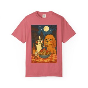 Puede incluir: Camiseta rosa polvoriento con una ilustraci&oacute;n de dos perros compartiendo espaguetis. La escena incluye una botella de vino, una vela encendida y una luna llena en el cielo nocturno. Los perros tienen expresiones gru&ntilde;onas.