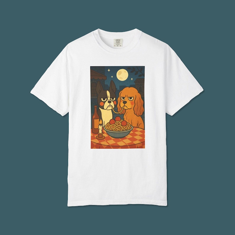 Puede incluir: Camiseta blanca con una ilustraci&oacute;n de dibujos animados de dos perros compartiendo espaguetis. Uno es blanco y negro, el otro es marr&oacute;n. Una botella de vino y una vela encendida est&aacute;n sobre la mesa. El fondo muestra una escena nocturna con luna llena.