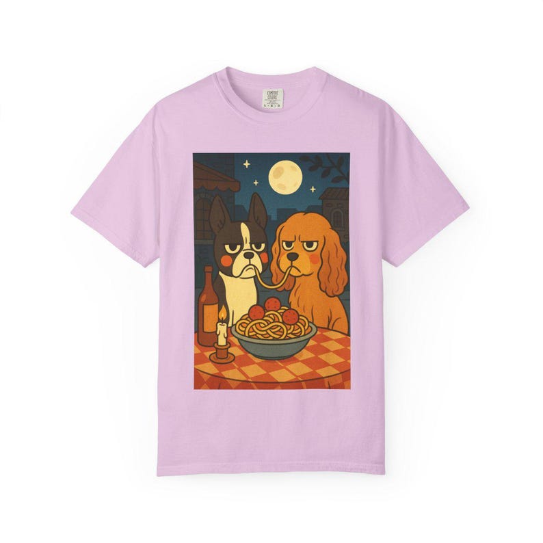 Puede incluir: Camiseta de color lila claro con una ilustraci&oacute;n de dibujos animados de dos perros compartiendo espaguetis. La escena incluye una botella de vino, una vela encendida y una luna llena. Los perros tienen expresiones de mal humor.
