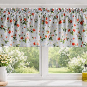 May include: A light blue kitchen valance with a repeating pattern of red strawberries and green leaves. The valance is gathered at the top and hangs above a window. The window overlooks a garden scene.