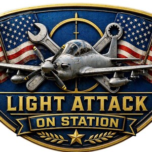 May include: A rectangular metal sign with a gold border featuring a silver propeller aircraft centered over crossed wrenches and a target reticle. Two American flags flank the plane. The text reads LIGHT ATTACK ON STATION above a gold star and laurel.