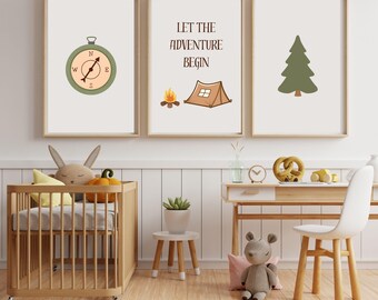 May include: Three framed prints with a camping theme. One print features a compass, another says "Let the Adventure Begin" with a tent and campfire, and the third shows a pine tree. The prints are in a light-colored room with a crib and desk.