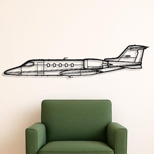 May include: A black metal wall art piece depicting a jet airplane. The artwork is a line drawing of the plane's silhouette, showing the fuselage, wings, and tail. The art is mounted on a white wall above a green armchair.