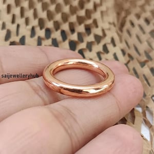 May include: A polished rose gold-toned ring with a smooth, rounded band and a simple circular design. The text saijewelleryhub is visible on the left side of the image. The ring features a reflective metallic surface with a warm, copper-like hue.