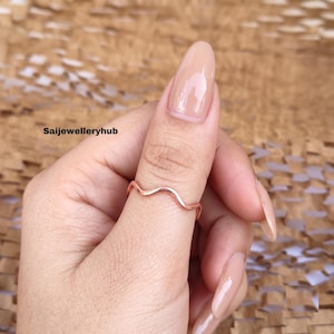 May include: A thin rose gold ring with a continuous wavy or serpentine design worn on the thumb. The metal has a smooth, polished finish. The text Saijewelleryhub is visible in the upper left corner of the image, indicating the brand name.
