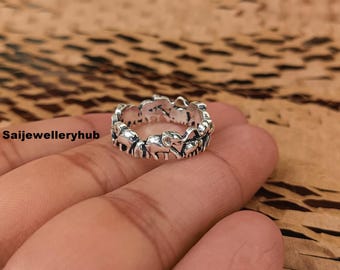 May include: A silver ring featuring a repeating elephant design. The ring is detailed with small elephant figures around the band. The ring is shown on a hand against a brown background.