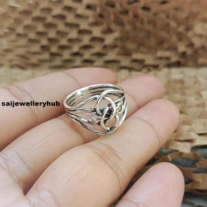 Op de afbeelding: Een zilverkleurige ring met een ingewikkeld Keltisch knoopontwerp. De ring heeft een reeks van verweven lijnen en lussen, waardoor een complex patroon ontstaat. De ring is waarschijnlijk gemaakt van sterling zilver. De tekst "saijewelleryhub" is zichtbaar.