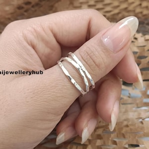 Peut inclure: Une bague en argent au design multi-anneaux avec une finition martelée et texturée. La bague se compose de trois bandes interconnectées qui s'enroulent autour du doigt. Le texte "saijewelleryhub" est visible sur le côté gauche de l'image.