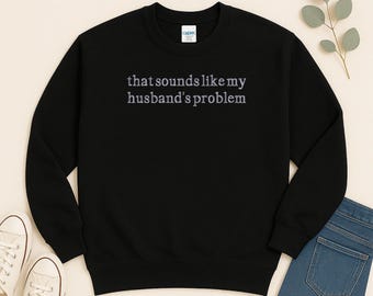 Może przedstawiać: Czarna bluza z okrągłym dekoltem z napisem "that sounds like my husband's problem" w jasnofioletowych literach. Bluza jest prezentowana na neutralnym tle z białymi trampkami i niebieskimi dżinsami.