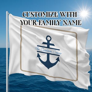 Op de afbeelding: Witte vlag met een marineblauw ankerontwerp en de tekst "The Custom Crew". De vlag heeft een touwrand en de tekst "Customize with your family name" staat bovenaan. De vlag wappert voor een blauwe zee en lucht.