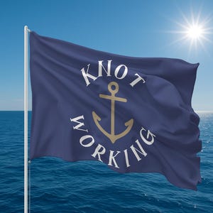 May include: A navy blue flag with the words "KNOT WORKING" in a circular design around a gold anchor. The flag is waving in the wind against a blue sky and ocean, with the sun shining brightly.