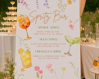 May include: A wooden easel displays a sign with "Spritz Bar" in gold script. The sign features watercolor illustrations of cocktails and floral accents. The menu lists Aperol, Hugo, and Limoncello Spritz recipes.