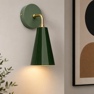 May include: A wall-mounted lamp featuring a dark green conical shade, a brass-colored curved arm, and a circular sage green wall plate. The light fixture emits a warm, downward-facing glow from the open bottom of the glossy green metal cone.