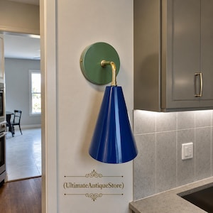 May include: A wall-mounted light fitting featuring a circular sage green backplate and a glossy royal blue conical shade. The shade is connected to the backplate by a curved brass-toned metal arm. The text UltimateAntiqueStore is visible below.