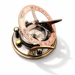 Könnte beinhalten: Eine kreisförmige Sonnenuhr-Kompass-Kombination aus Messing mit einem aufklappbaren Kupferring, römischen Ziffern und der Gravur Gilbert & Sons London. Das Gerät verfügt über einen zentralen Magnetkompass mit Nadel und einen klappbaren Gnomon.