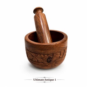 Puede incluir: Un juego de mortero y mano de madera de color marrón oscuro que incluye una mano cilíndrica lisa y un cuenco con una banda tallada y texturizada en el exterior. El texto "Ultimate Antique 1" está impreso en negro debajo del utensilio de cocina.